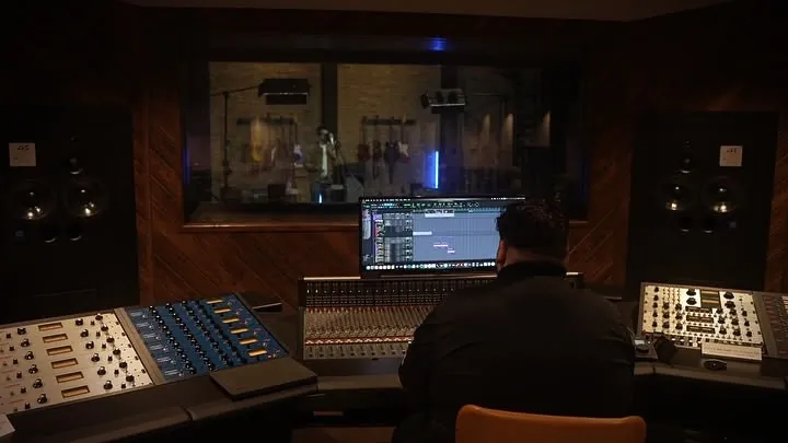 Big Ro Muzic mixing at a studio console in front of a live room